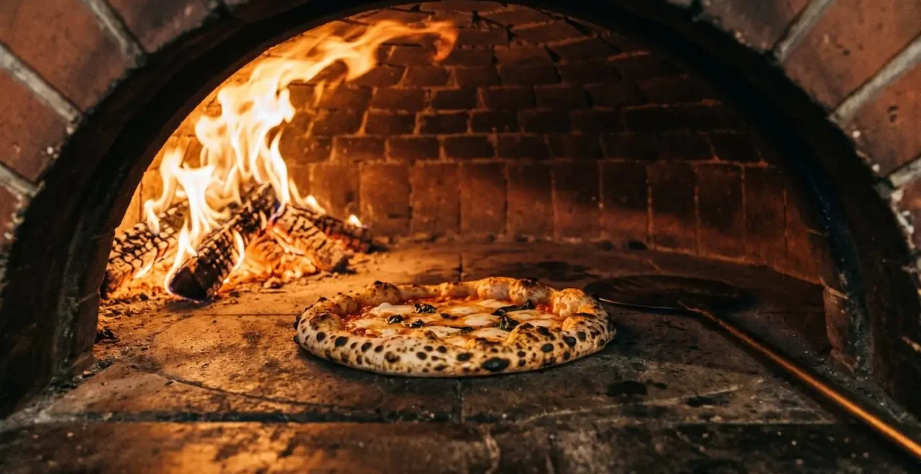 Intérieur d'un four à bois napolitain avec pizza en cuisson sur sole en pierre, flammes vives sur le côté et taches léopardées sur le bord de la pizza